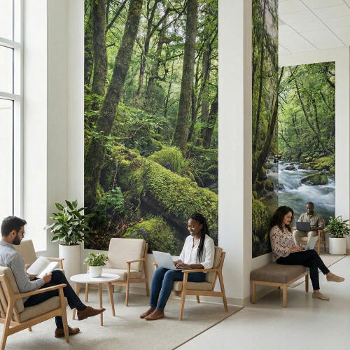 A bright, modern office lounge where professionals sit in light wood armchairs using laptops and reading. The space is defined by three large, vertical forest murals showing mossy trees and a flowing river. Potted plants and a large window are visible.